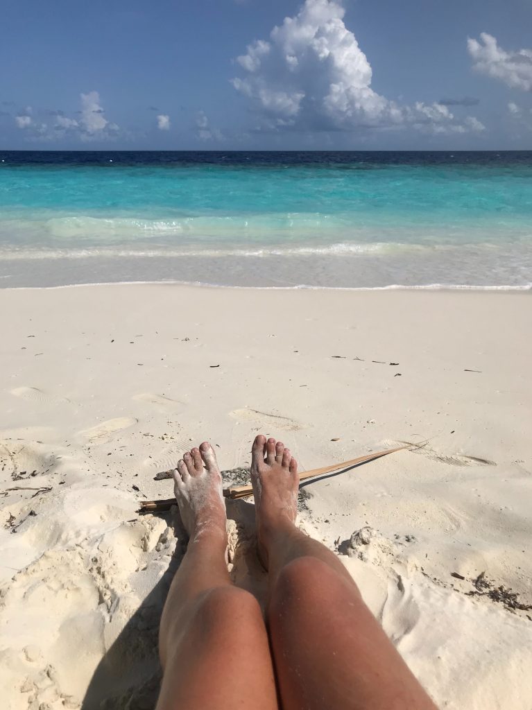 pogoda na Malediwach, biały piasen, kobiece nogi na piasku, turkusowa spokojna woda